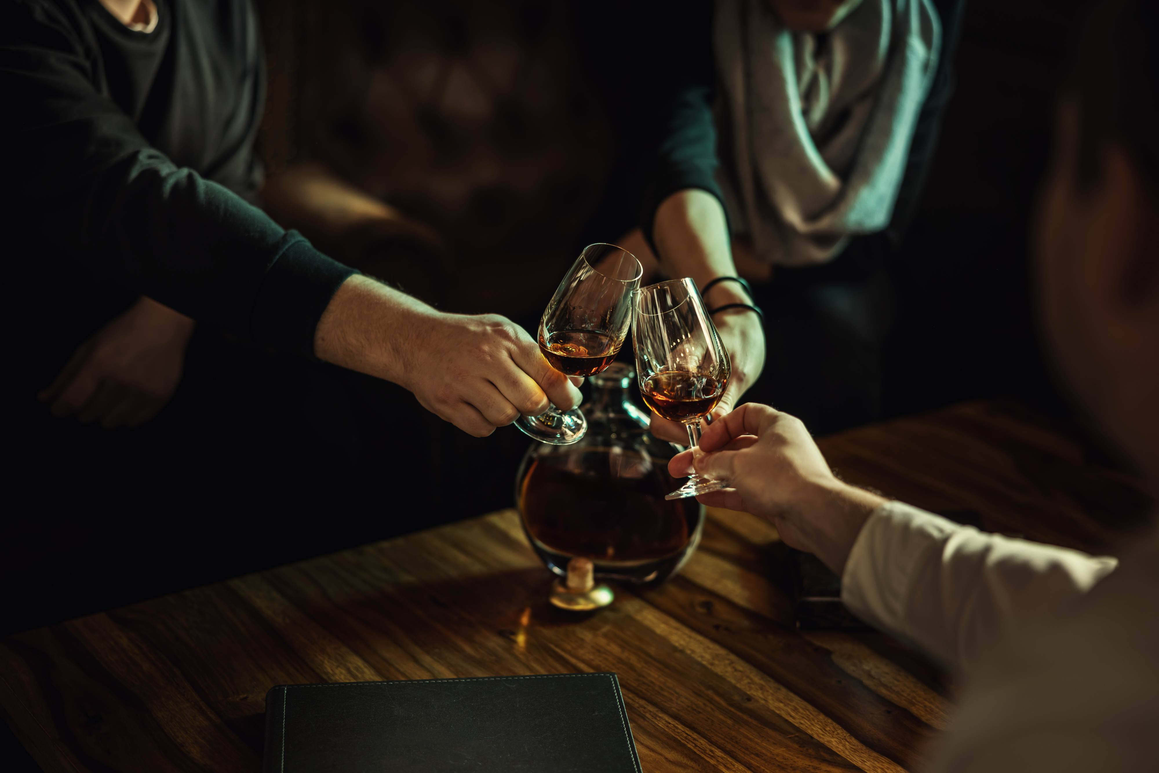 Four people clinking glasses in a toast at a dimly lit table
