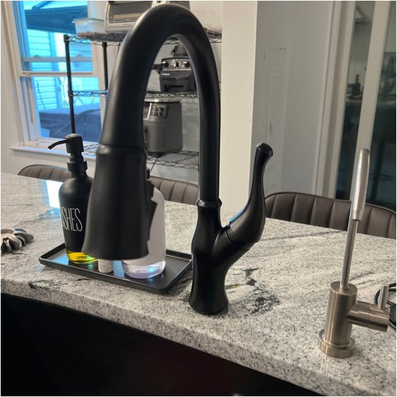 A kitchen faucet with a soap dispenser and a bottle labeled &#x27;DISHES&#x27; on a countertop, with a window in the background