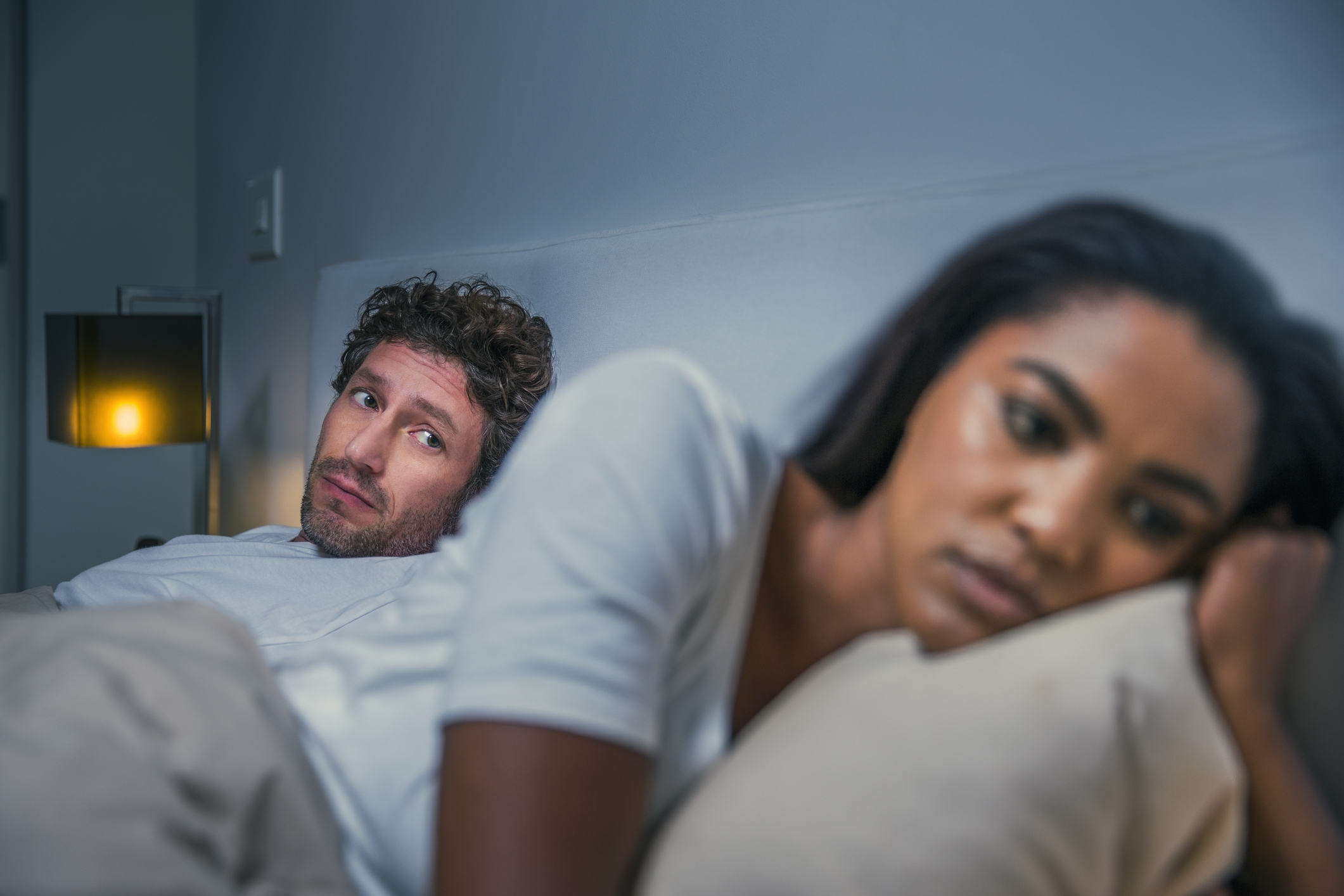 A couple in bed looking away from each other, appearing upset and distant