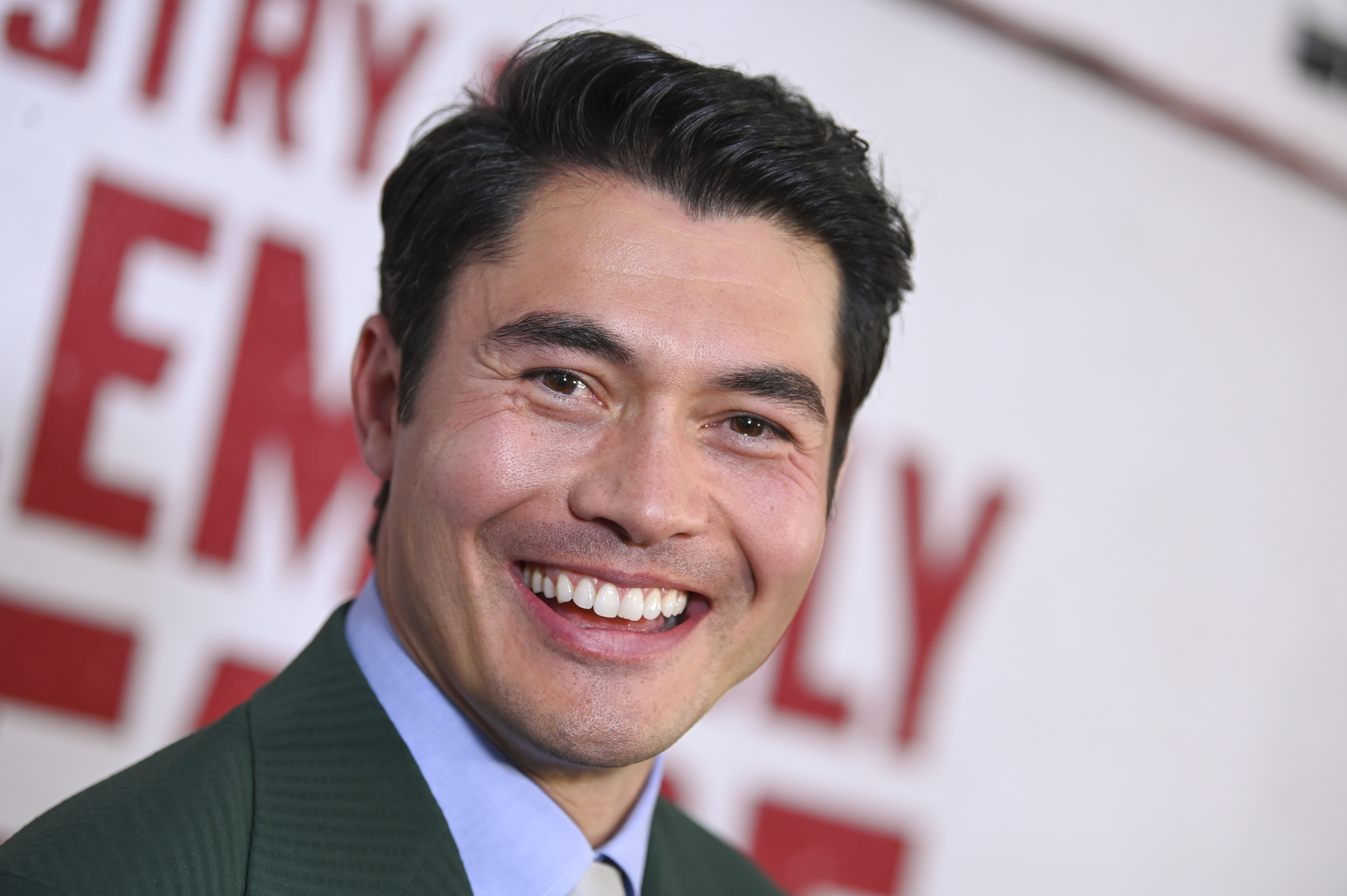 Henry Golding a suit smiling at a camera on a red carpet