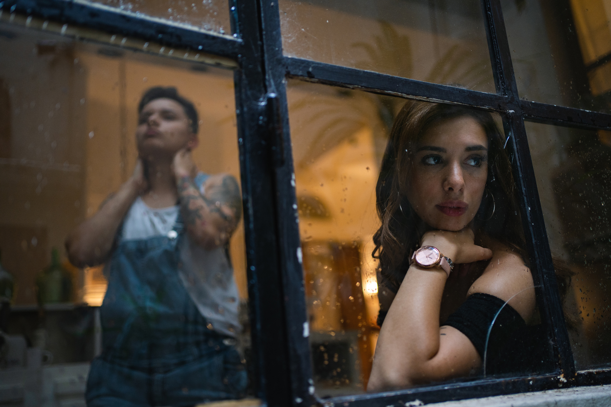 A man shaves by a window while a woman gazes outward, reflecting on their relationship