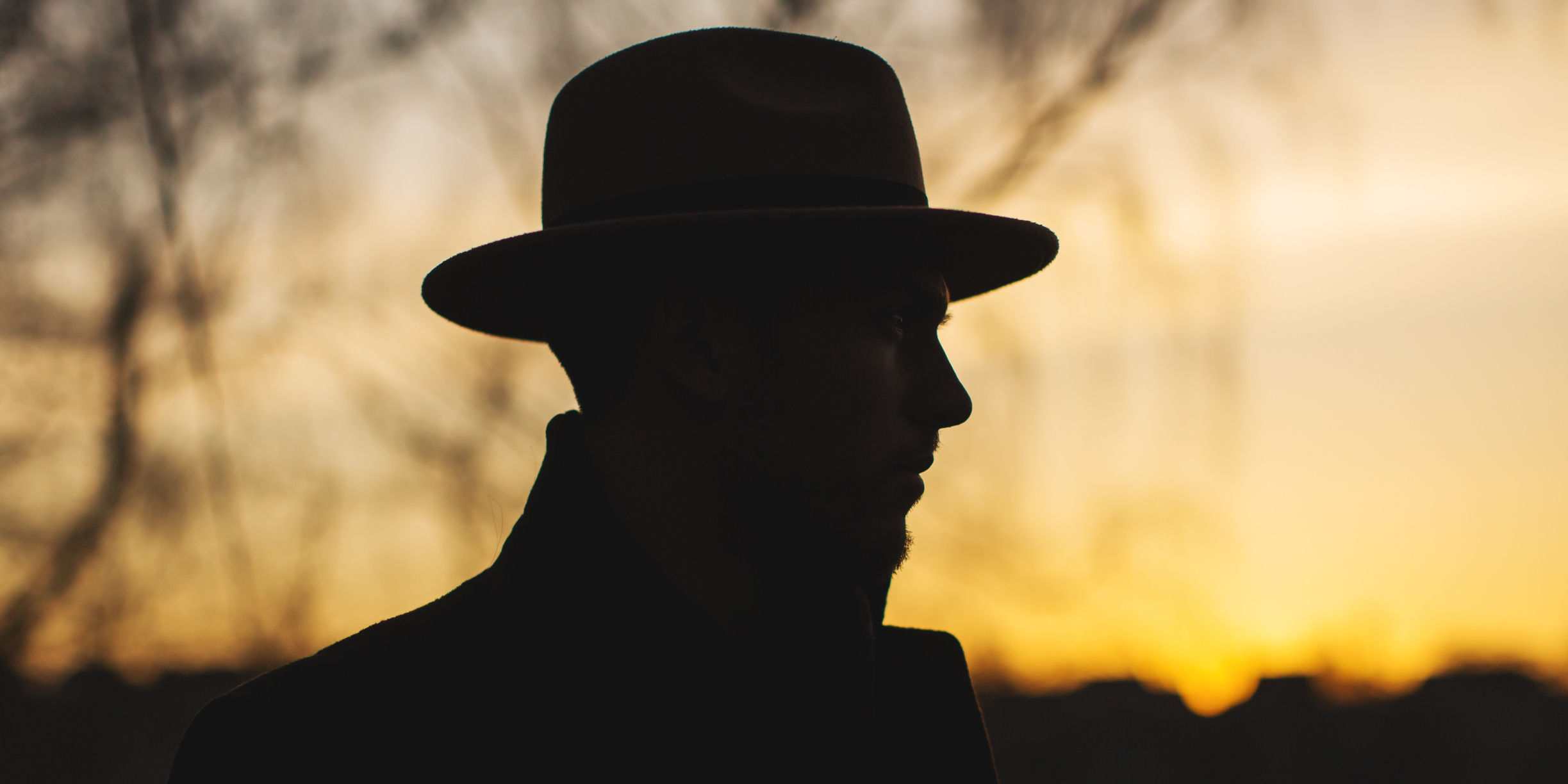 Silhouette of a person wearing a fedora hat against a sunset backdrop