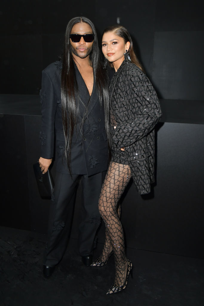 Law Roach and Zendaya pose together; Zendaya wears a stylish dress with patterned tights and heels