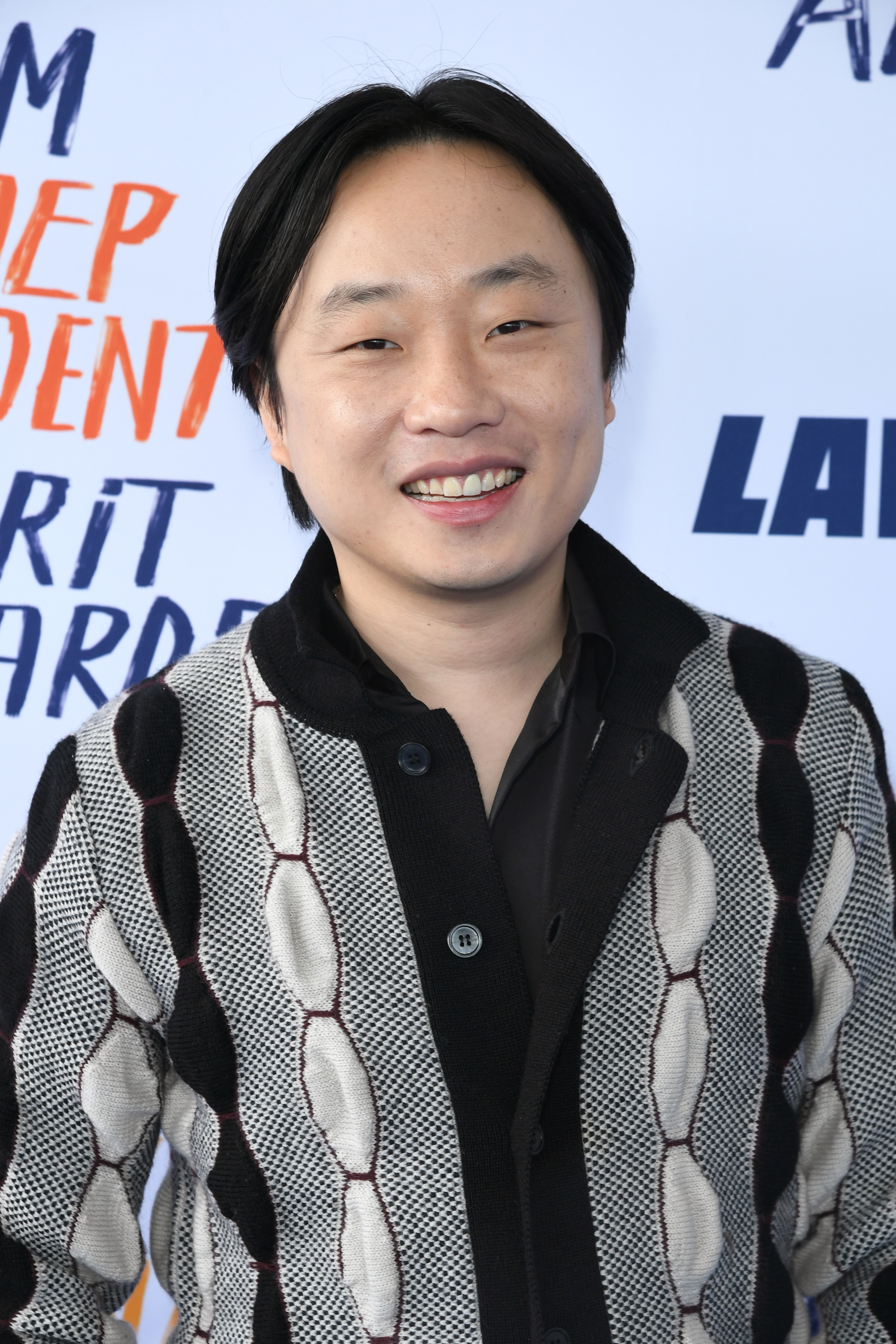 Jimmy O. Yang in patterned black and white jacket over black shirt smiles for camera at event