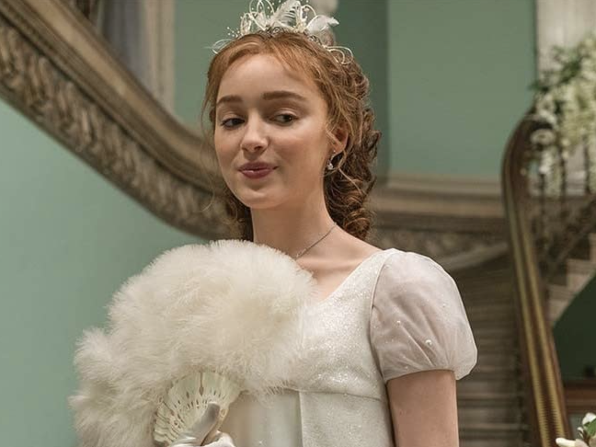 Personaje de Bridgerton (Daphne) con vestido de época y abanico, en interior elegante