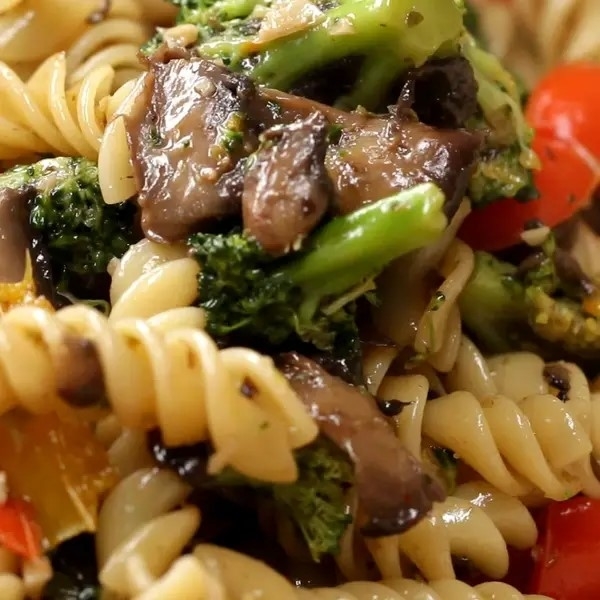 Close-up of pasta with broccoli, mushrooms, and red peppers, implying a flavorful dish