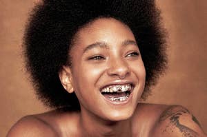 Smiling person with afro hairstyle and a visible grill on their teeth, posing for the camera