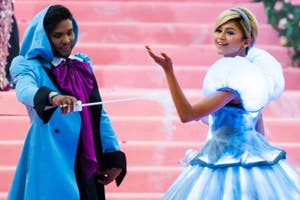 Zendaya in a ballgown and an actor as Prince Charming in costume posing playfully at an event