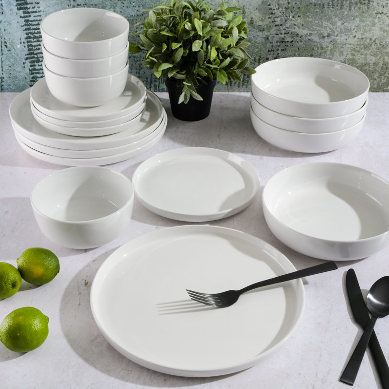 A variety of white dinnerware including plates, bowls, and a serving dish on a table with a black fork