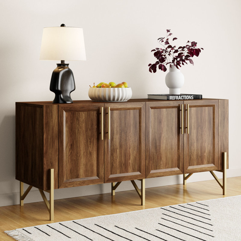 A wooden sideboard with metal legs, a lamp, decorative vase, fruit bowl, and a book
