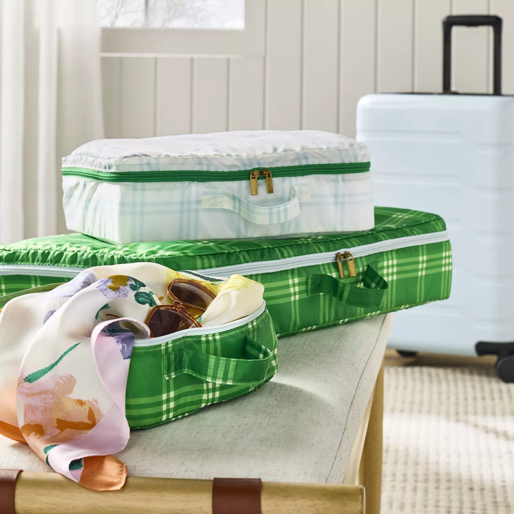 Stacked plaid patterned packing cubes with clothes on a bench, suggesting an organized travel packing solution