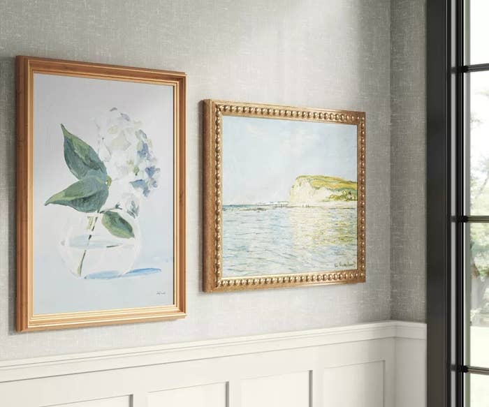 Two framed paintings on a wall, one depicting flora and the other a seaside landscape