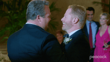 Two men in formal wear embracing and laughing at a festive event