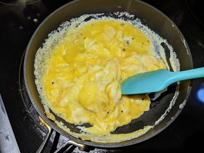 Scrambled eggs cooking in a nonstick skillet, being stirred with a blue spatula