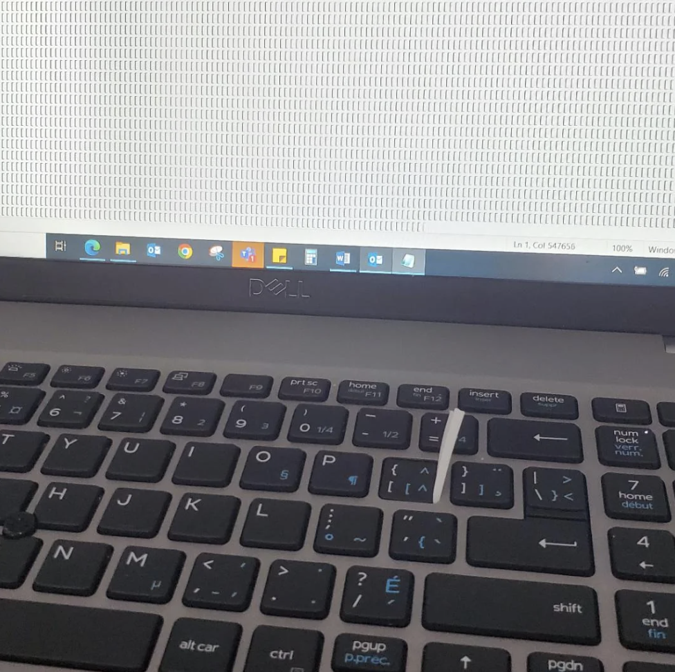 A close-up of a Dell laptop with a document open, showing a large number of repeated text characters on the screen