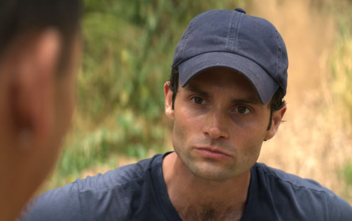 A man wearing a baseball cap and a t-shirt is having a serious conversation outdoors