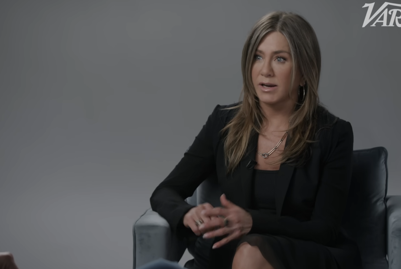 Jennifer Aniston in a black outfit sits on an armchair speaking during a Variety interview, with &quot;Variety&quot; branding in the top right corner