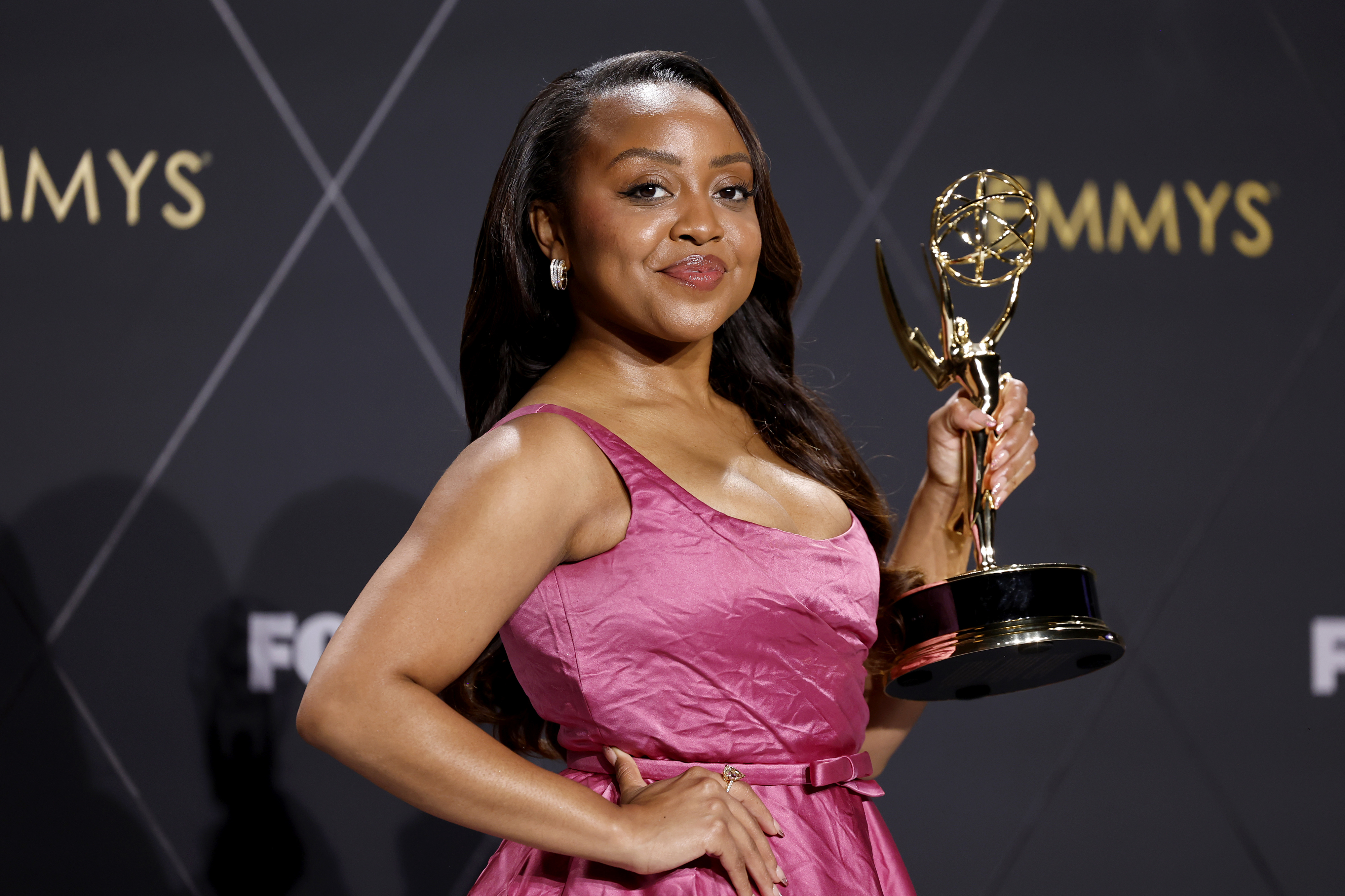 Quinta Brunson holds an Emmy award, wearing a stylish dress, while posing for a photo at the Emmys