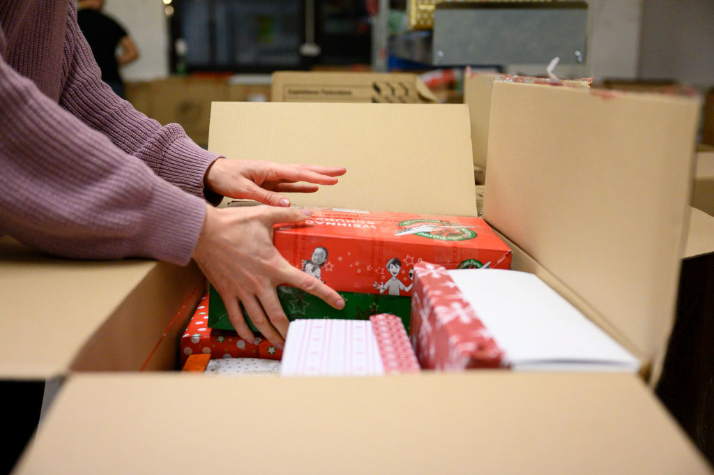 Hands placing wrapped gifts into an open cardboard box, preparing for shipment or delivery