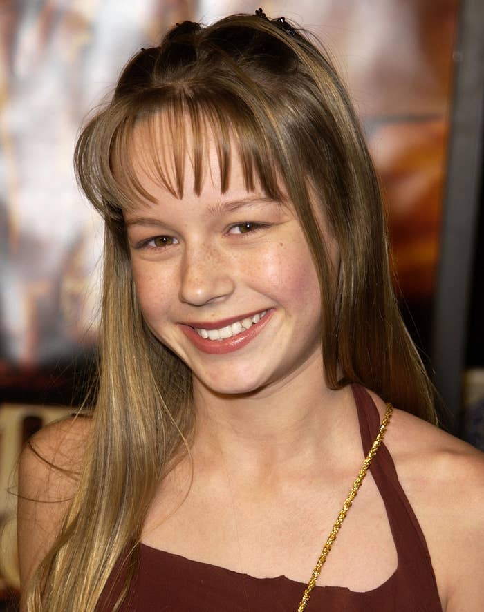 A teenage Brie Larson with long hair and bangs, smiling at the camera