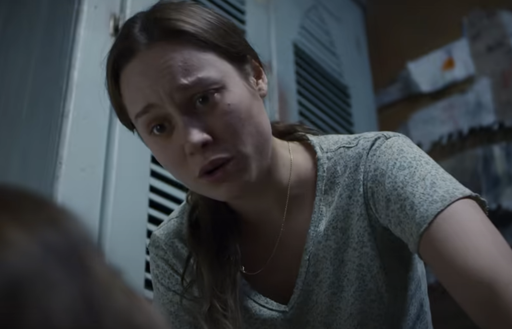 Brie Larson looks concerned while leaning over, wearing a patterned T-shirt and a necklace