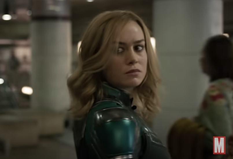 Brie Larson, as Captain Marvel, looks intently over her shoulder in an action scene, wearing her character&#x27;s signature armored suit