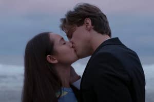 Lola Tung and Christopher Briney share a kiss at the beach with the ocean in the background as Belly and Jeremiah on The Summer I Turned Pretty