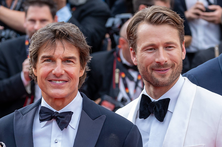 Tom Cruise and Glen Powell at a red carpet event, both wearing tuxedos with bow ties, surrounded by photographers