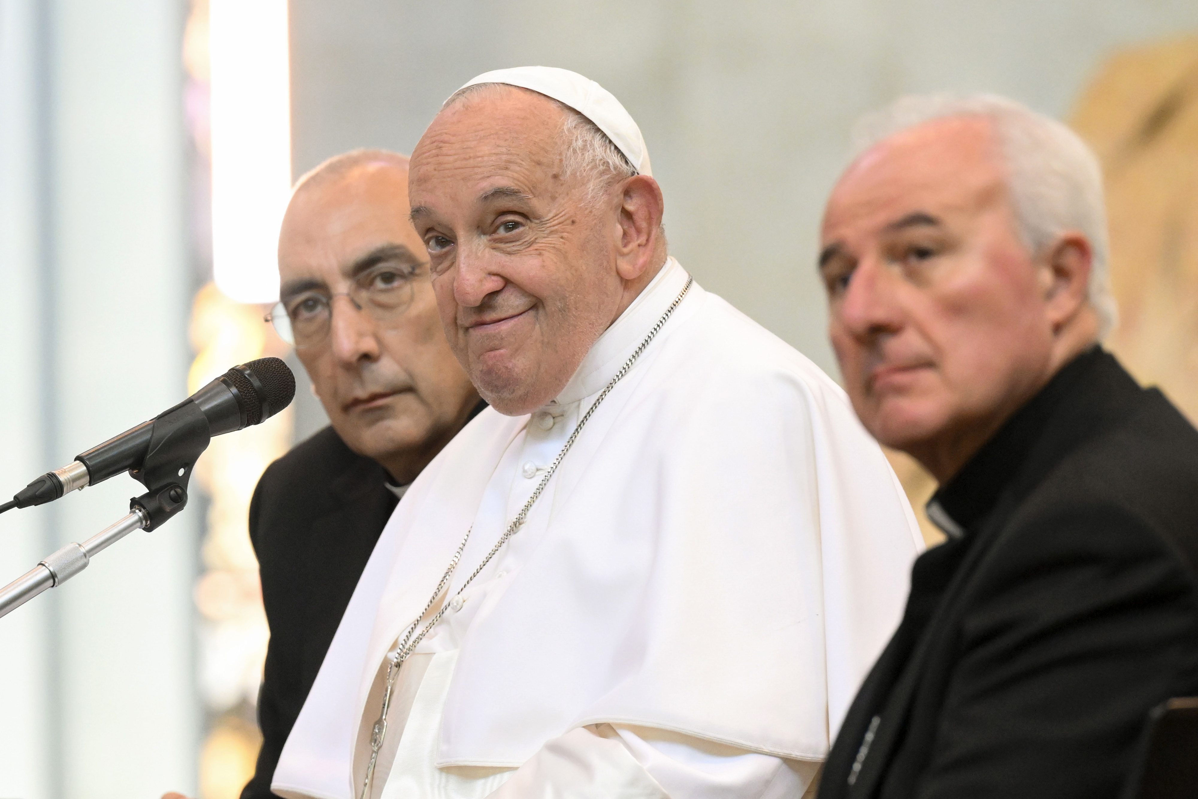 Pope Francis sits between two clergy members in a public event