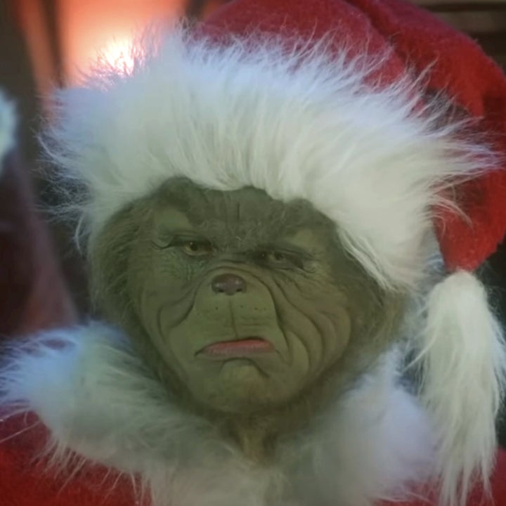 The Grinch dressed as Santa Claus, wearing a fluffy red suit and hat, looking grumpy