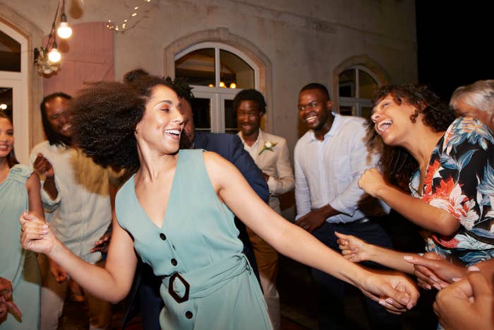 Group of radical dancing and smiling astatine a lively party. Several individuals are dressed successful festive attire, with 1 pistillate successful a sleeveless formal successful the foreground