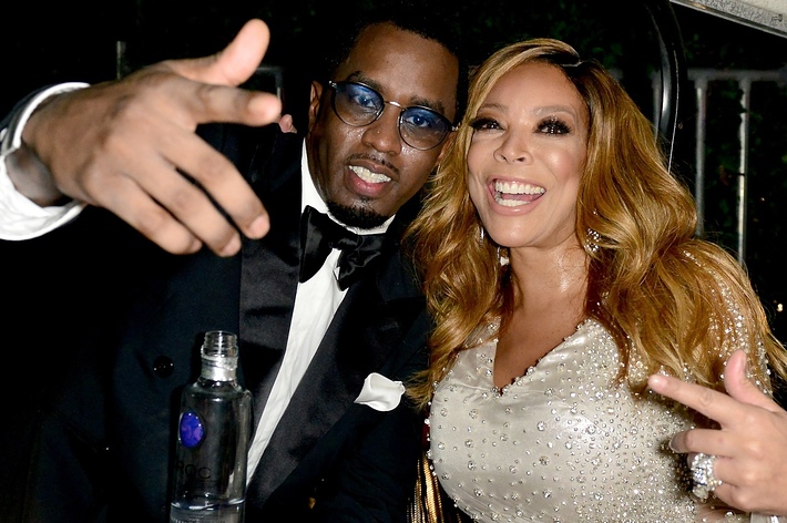 Sean “Diddy” Combs in a black tuxedo and Wendy Williams in a sequined dress smile and gesture at the camera