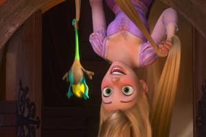 Rapunzel, from Tangled, hangs upside down with her hair touching the floor, while Pascal, her chameleon, swings from her hair. She looks cheerful