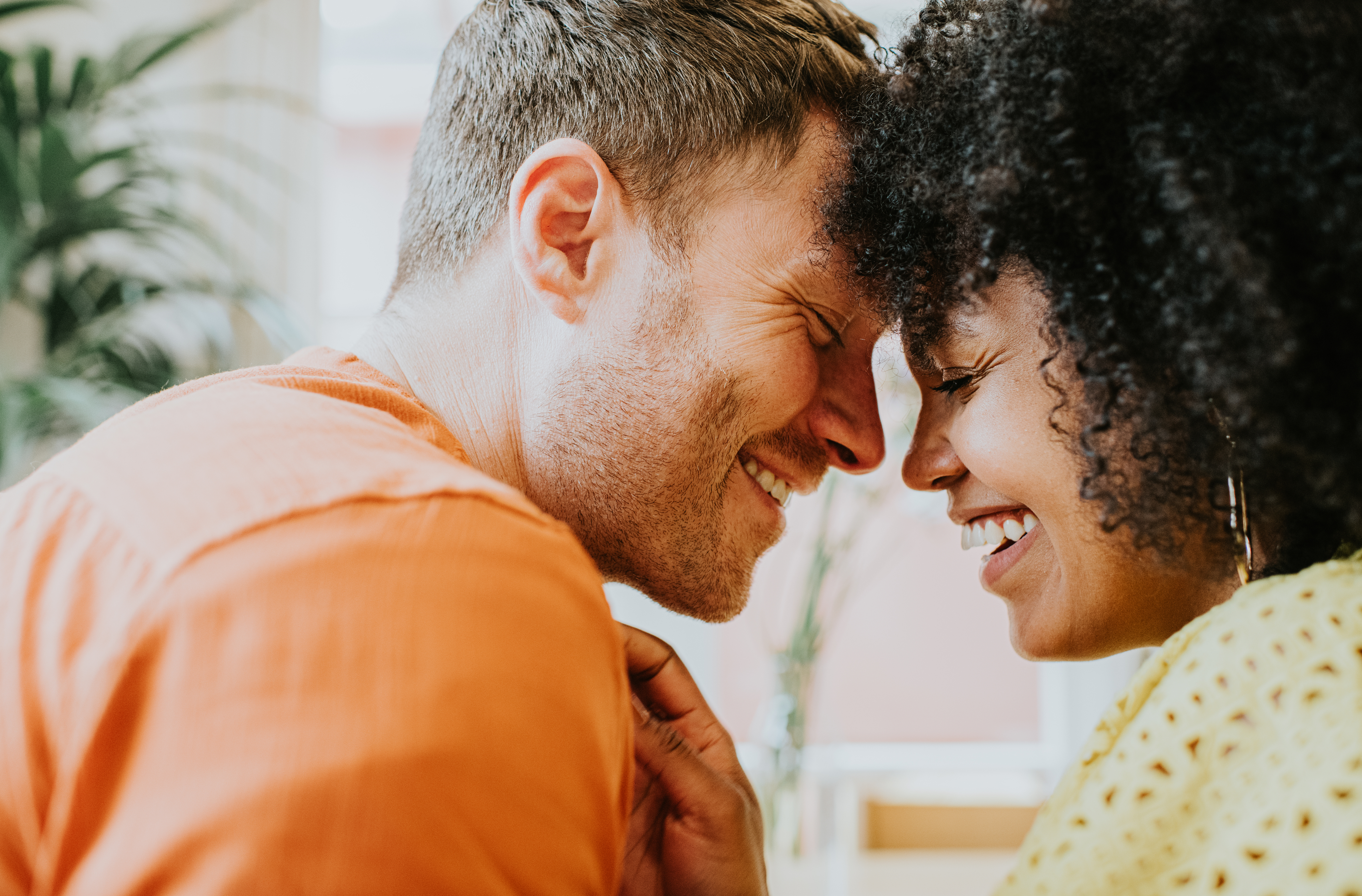 A couple, smiling broadly, touches foreheads affectionately in a close embrace