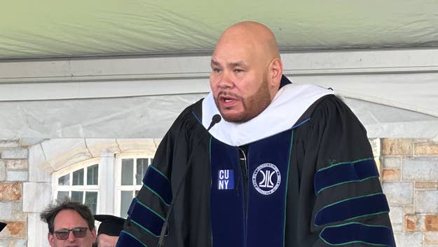 Fat Joe delivering a commencement speech at a graduation ceremony, wearing a traditional academic gown and hood on stage