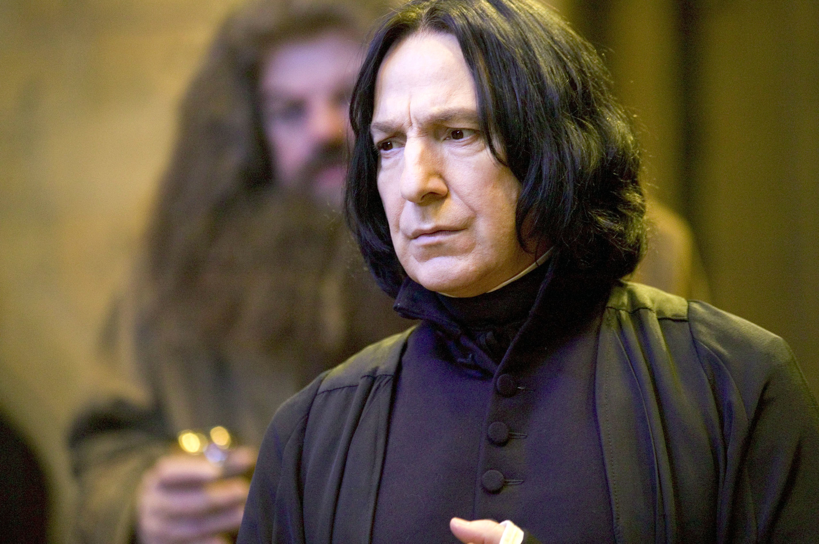 Severus Snape in a black robe standing in the foreground, with Rubeus Hagrid blurred in the background