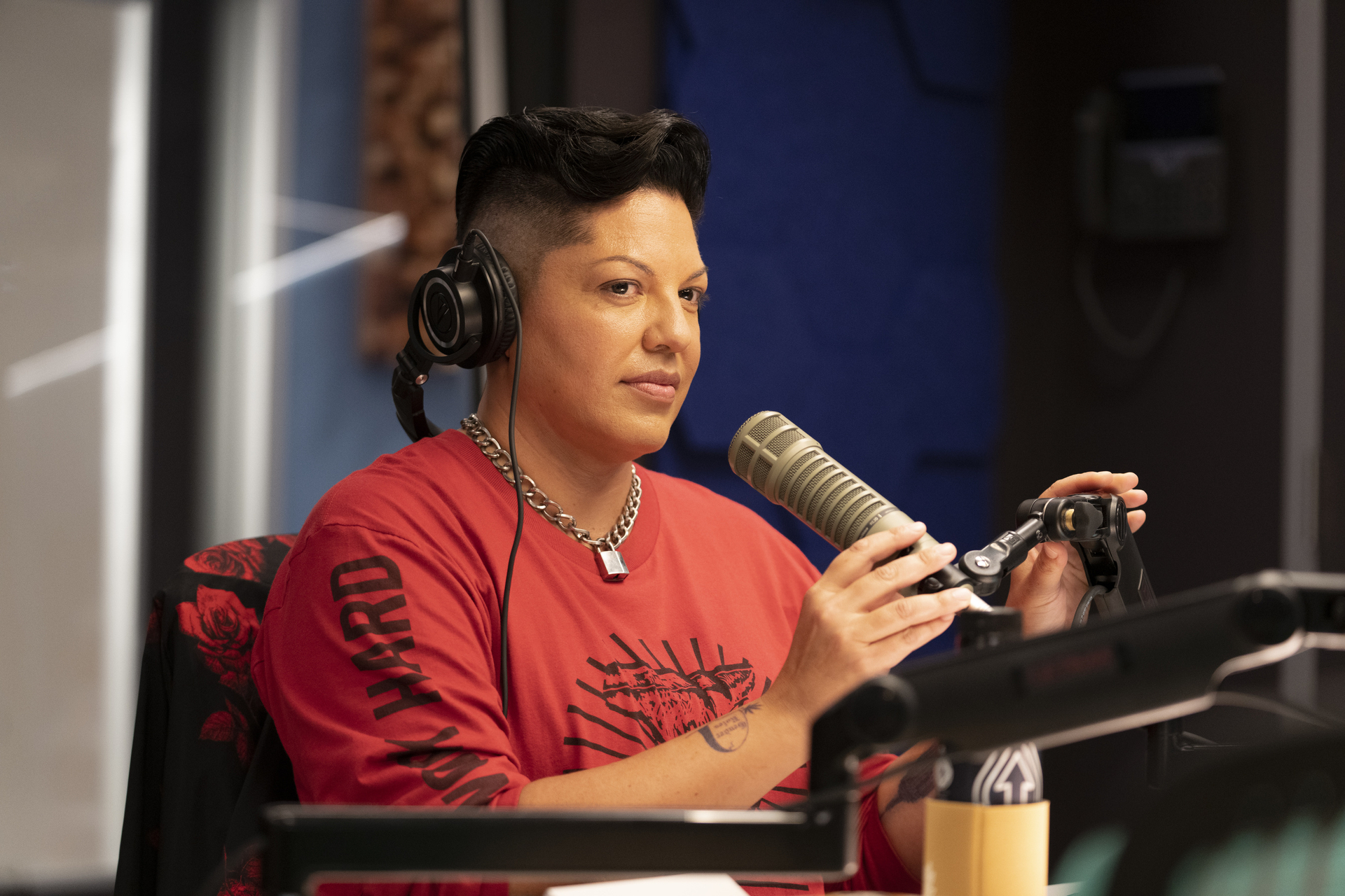 Sara Ramirez, wearing a casual long-sleeve shirt and headphones, speaks into a microphone during a radio interview