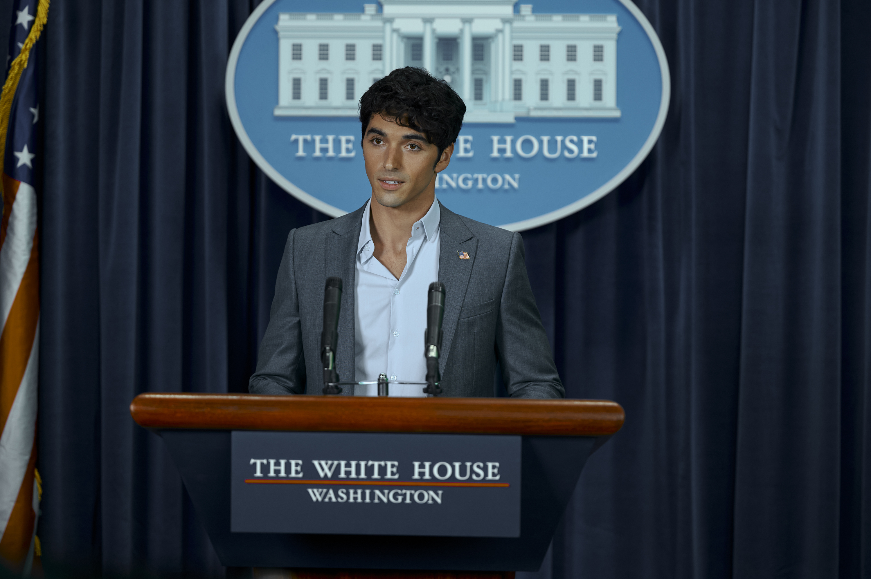 Young man stands at a podium labeled &quot;The White House Washington&quot; speaking in front of a backdrop with the same text and the White House image