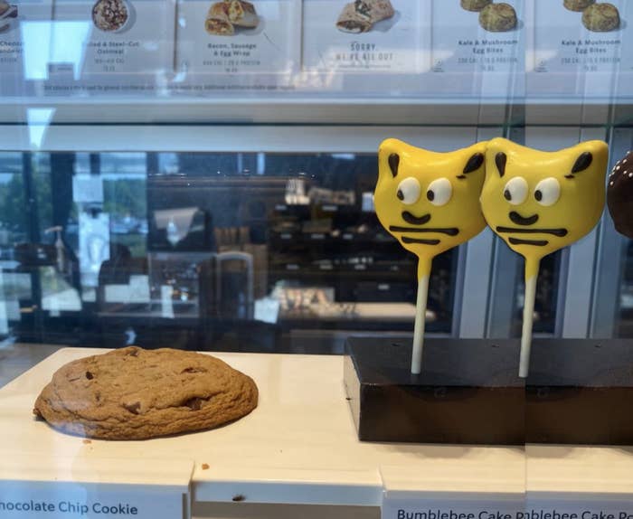 A chocolate chip cookie is displayed on the left, and two yellow bear-shaped cake pops with facial expressions are on the right in a pastry case