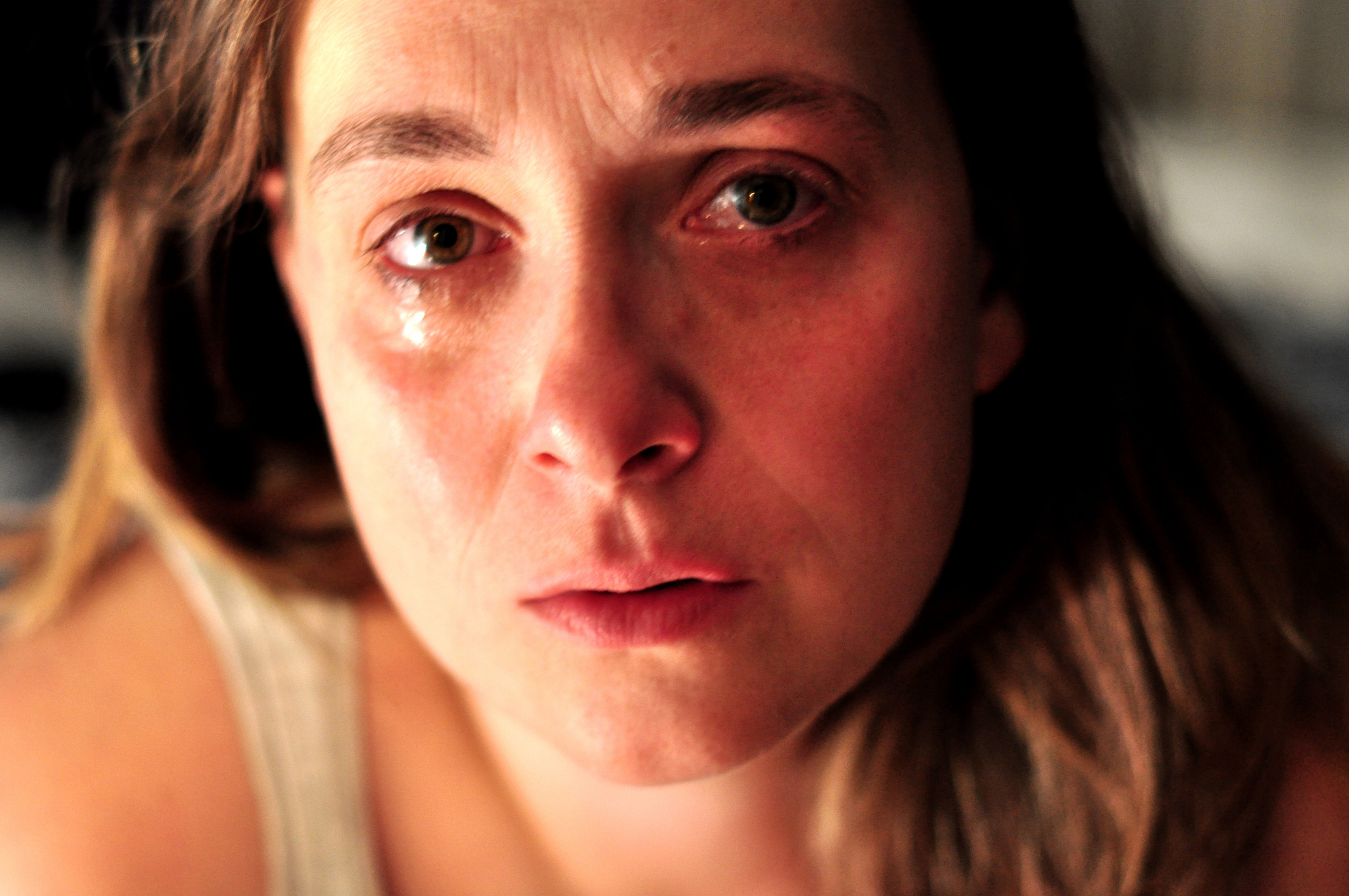 A woman with teary eyes and a solemn expression looks directly at the camera