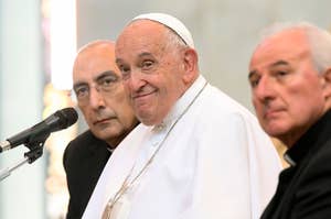 Pope Francis sits between two clergy members in a public event