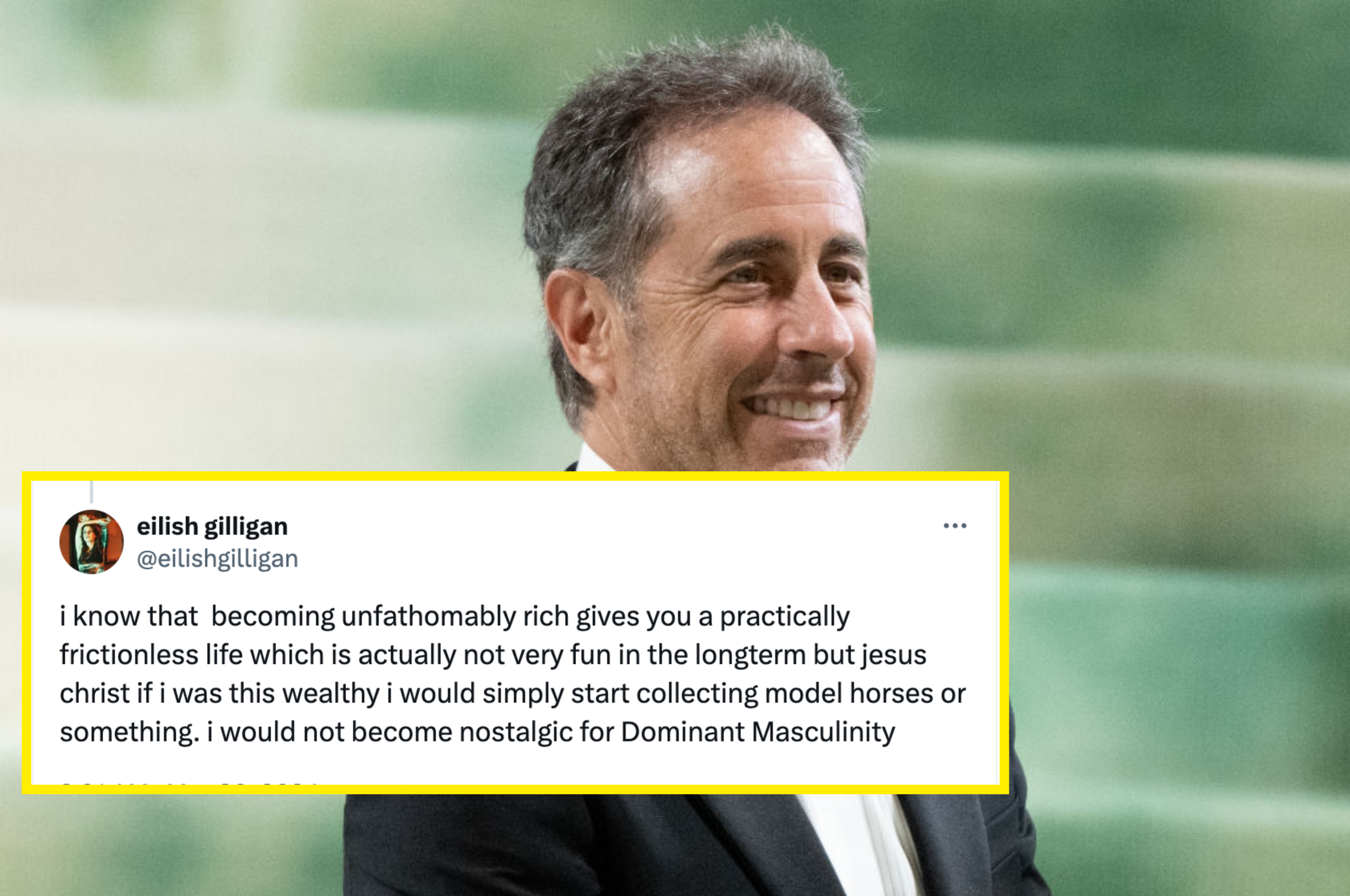 Jerry Seinfeld sits on a sofa during an interview, wearing a pinstripe blazer and a light-colored shirt. A colorful backdrop is behind him