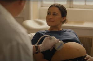 A pregnant woman lies on a medical bed while a doctor conducts an ultrasound. She smiles and looks up at the doctor. The scene conveys a check-up during pregnancy