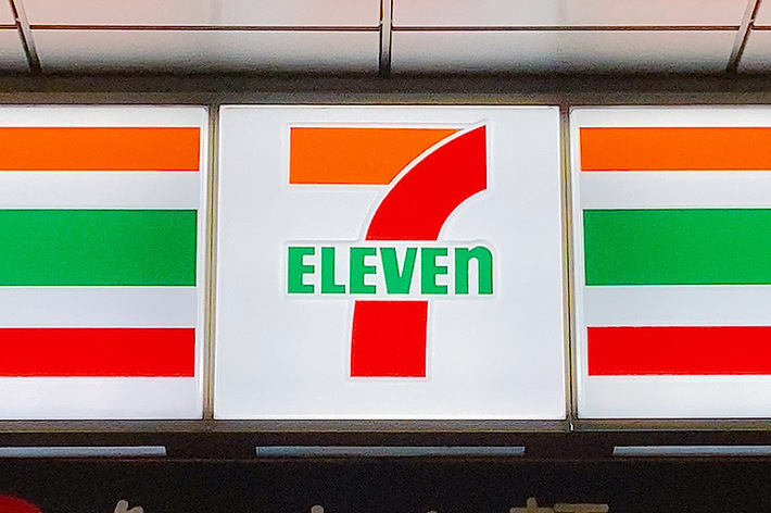 セブンイレブンの看板と「あったか麺 さらにコシ強く、つゆ香る」の広告が写っている店舗の正面。