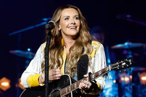 Carly Pearce performing on stage, smiling and playing a guitar, dressed in a stylish outfit with fringe details