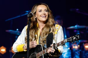 Carly Pearce performing on stage, smiling and playing a guitar, dressed in a stylish outfit with fringe details