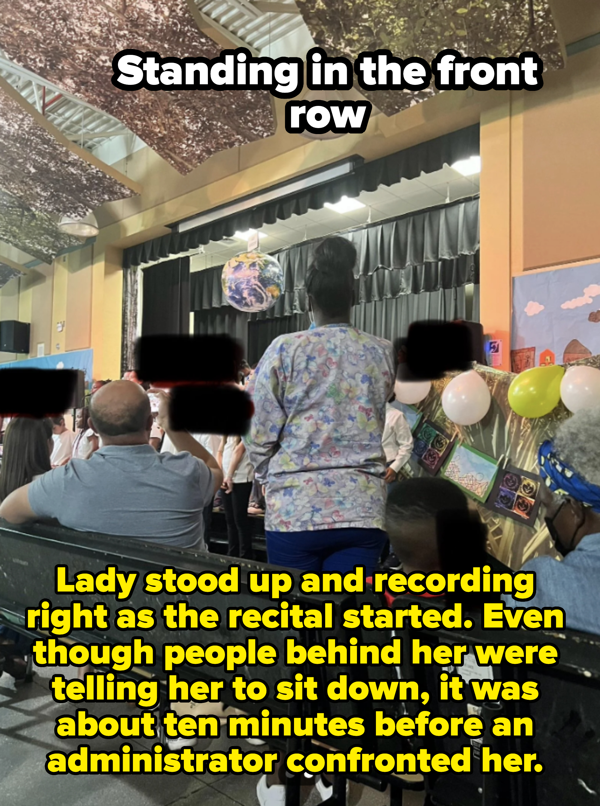 Audience members seated and standing in a school auditorium, watching a stage performance