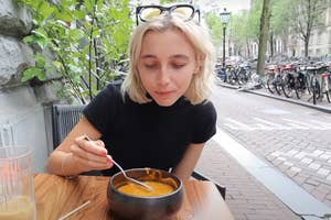 Emma Chamberlain sitting at an outdoor table with a bowl of soup in Amsterdam