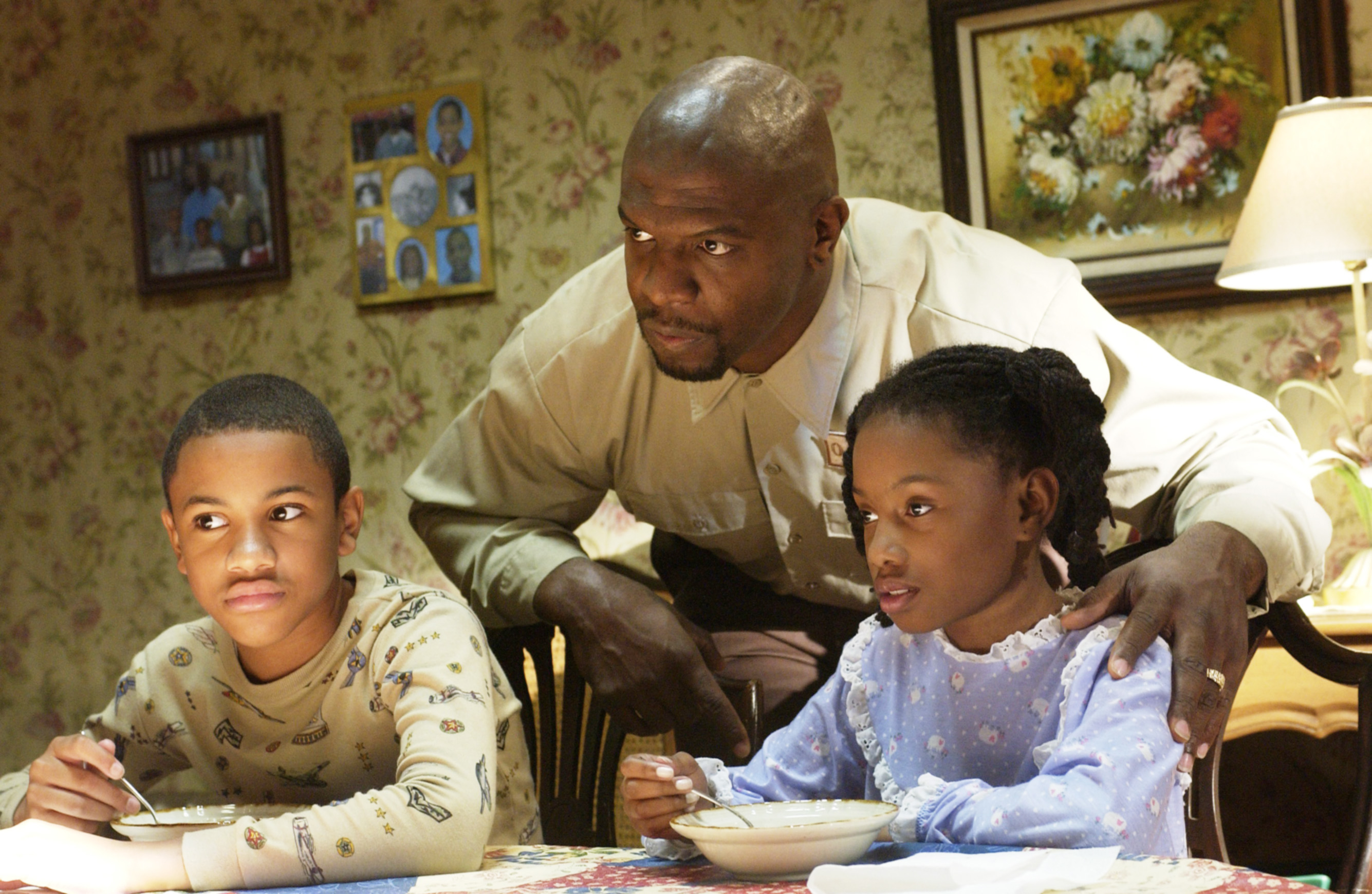 Tequan Richmond, Terry Crews, Imani Hakim at a kitchen table with floral wallpaper and photos hanging in the background