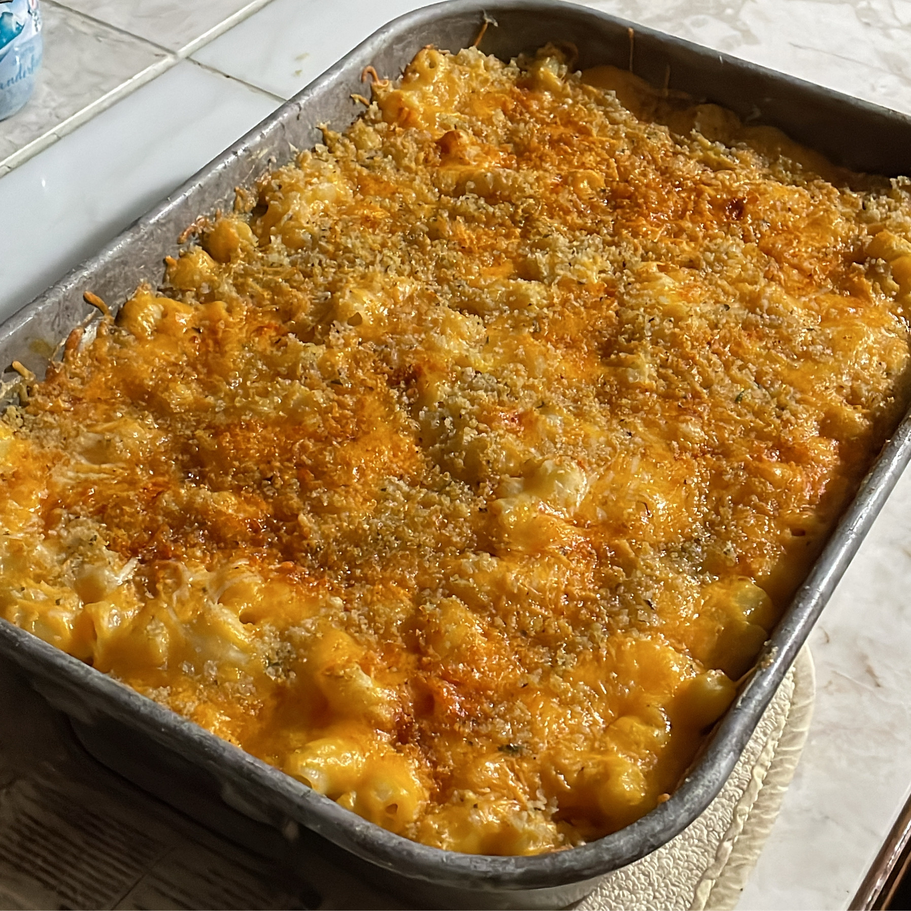 Baked mac and cheese cooling on a countertop in a metal pan, with a golden, crispy breadcrumb topping